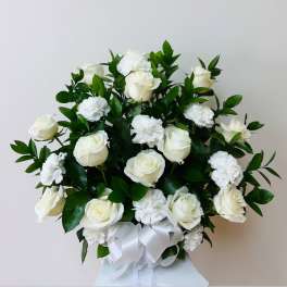 White roses and carnations arranged with a white ribbon bow