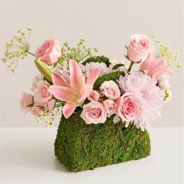 Pink roses and lilies arranged in a moss-covered container
