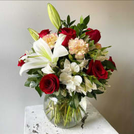 Bouquet of red roses, white lilies, and pale carnations in a glass vase