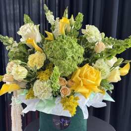 Yellow and white floral arrangement in a green hatbox