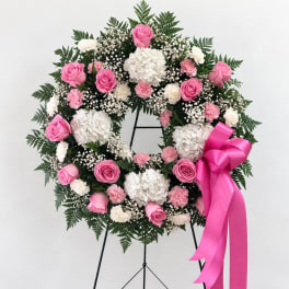 Pink and white floral wreath on a stand with a bright pink ribbon