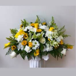 Yellow and white floral arrangement in a white pedestal vase