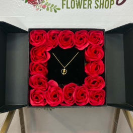 Red roses arranged in a black gift box around a necklace