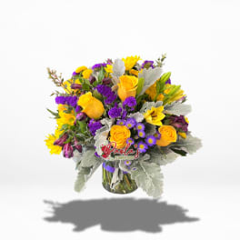 Bouquet of yellow roses, purple flowers, and lilies in a glass vase