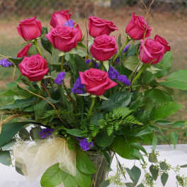 Pink roses arranged in a clear glass vase with purple filler flowers