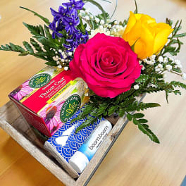 Gift tray with roses, purple flowers, and wellness items in a wooden box