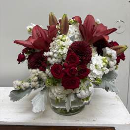 Red lilies and roses arranged in a clear glass vase with white blooms