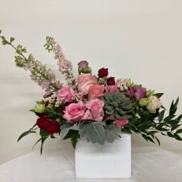 Pink and red roses with succulents in a white square vase