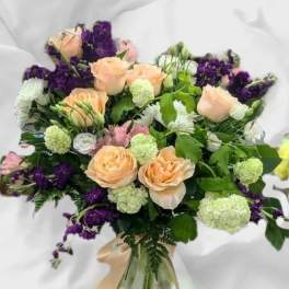 Peach roses and purple flowers in a glass vase with a ribbon