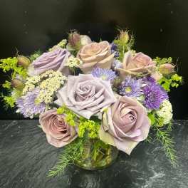 Lavender and blush roses with purple daisies in a glass vase