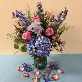 Blue and pink mixed bouquet in a glass vase with scattered petals