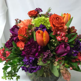 Mixed bouquet of orange, purple, and lime flowers in a glass vase