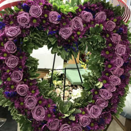 Heart-shaped floral wreath with purple roses and daisies on an easel