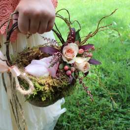 A person holds a rustic basket arrangement with roses and moss.