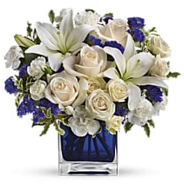 White lilies and roses in a blue glass vase with purple accents