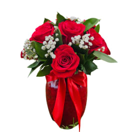 Red roses arranged in a glass vase with white filler flowers and a red ribbon