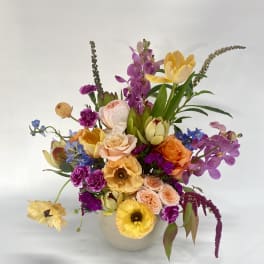 Colorful mixed bouquet in a white vase with orchids and roses