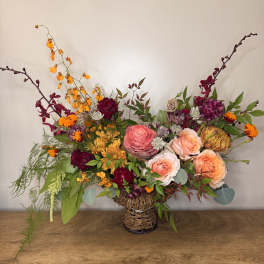 Mixed bouquet in a woven basket vase with roses and orange blooms