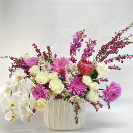 Mixed bouquet of white orchids, cream roses, pink dahlias, and purple orchids in a white vase