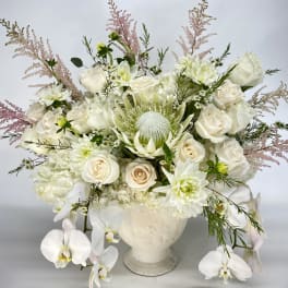 White floral arrangement in a cream vase with roses and orchids