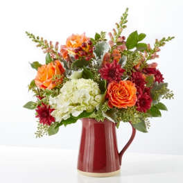 Mixed bouquet of orange, red, and white flowers in a red pitcher vase