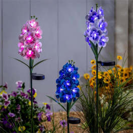 Set of three solar flower garden stakes with glowing pink, blue, and purple blooms in a garden bed.