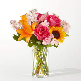 Bouquet of pink roses, orange lilies, and a sunflower in a glass vase