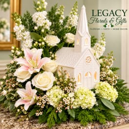 White floral arrangement with roses, lilies, and a church figurine