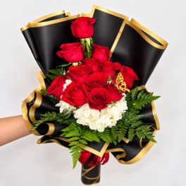 Bouquet of red roses and white hydrangeas wrapped in black paper with gold trim
