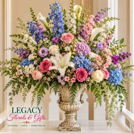 Large mixed floral arrangement in an ornate urn vase with roses, lilies, and blue blooms