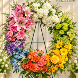 Large rainbow floral wreath on an easel with mixed blooms in pink, white, blue, orange, and yellow.