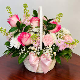 Pink roses and white daisies in a white basket with a pink ribbon