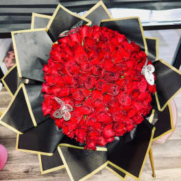 Round bouquet of red roses wrapped in black paper with gold trim