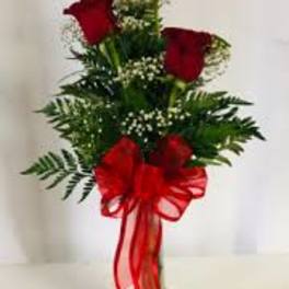 Red roses arranged in a clear vase with a large red bow