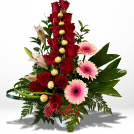 Tall arrangement of red roses, pink gerberas, and lilies with chocolates