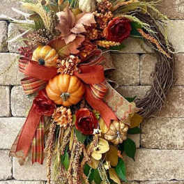 Autumn wreath with pumpkins, red roses, and ribbon on a stone wall