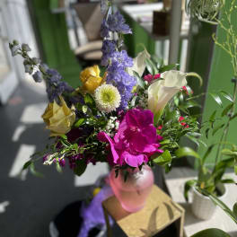 Mixed bouquet with purple, pink, yellow, and white flowers in a pink vase