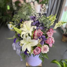 Bouquet of white lilies, pink roses, and purple flowers in a lavender hatbox