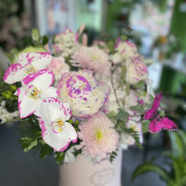 Pink and white orchid bouquet in a white vase with a butterfly accent