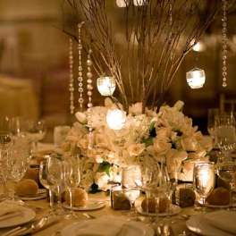 White floral centerpiece with hanging candle lights on a banquet table