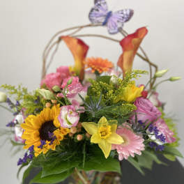 Mixed bouquet in a glass vase with sunflowers, pink blooms, and calla lilies