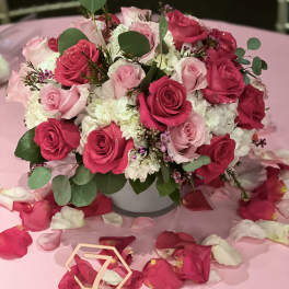 Pink and white rose arrangement in a white vase on a pink table