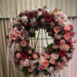 Large pink and white floral wreath on a stand with a ribbon bow