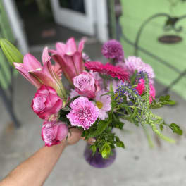 Handheld bouquet of pink roses, lilies, and mixed blooms in a purple vase