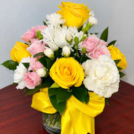 Yellow and pink roses with white daisies in a glass vase with a yellow ribbon