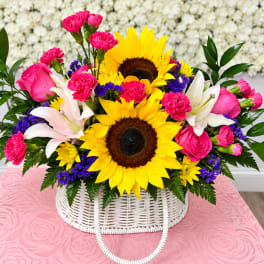 Bright bouquet with sunflowers, pink carnations, and white lilies in a white basket