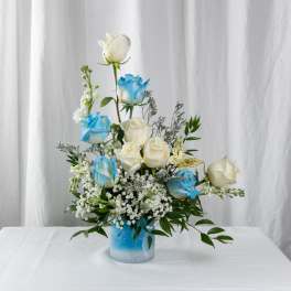 Blue and white roses arranged in a glass vase with greenery