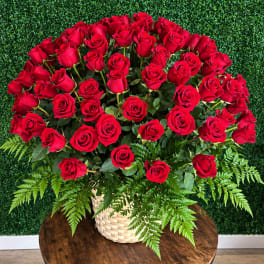 Large bouquet of red roses in a woven basket with fern foliage