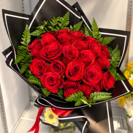 Bouquet of red roses wrapped in black paper with green fern accents