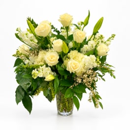 Cream roses and white flowers arranged in a clear glass vase